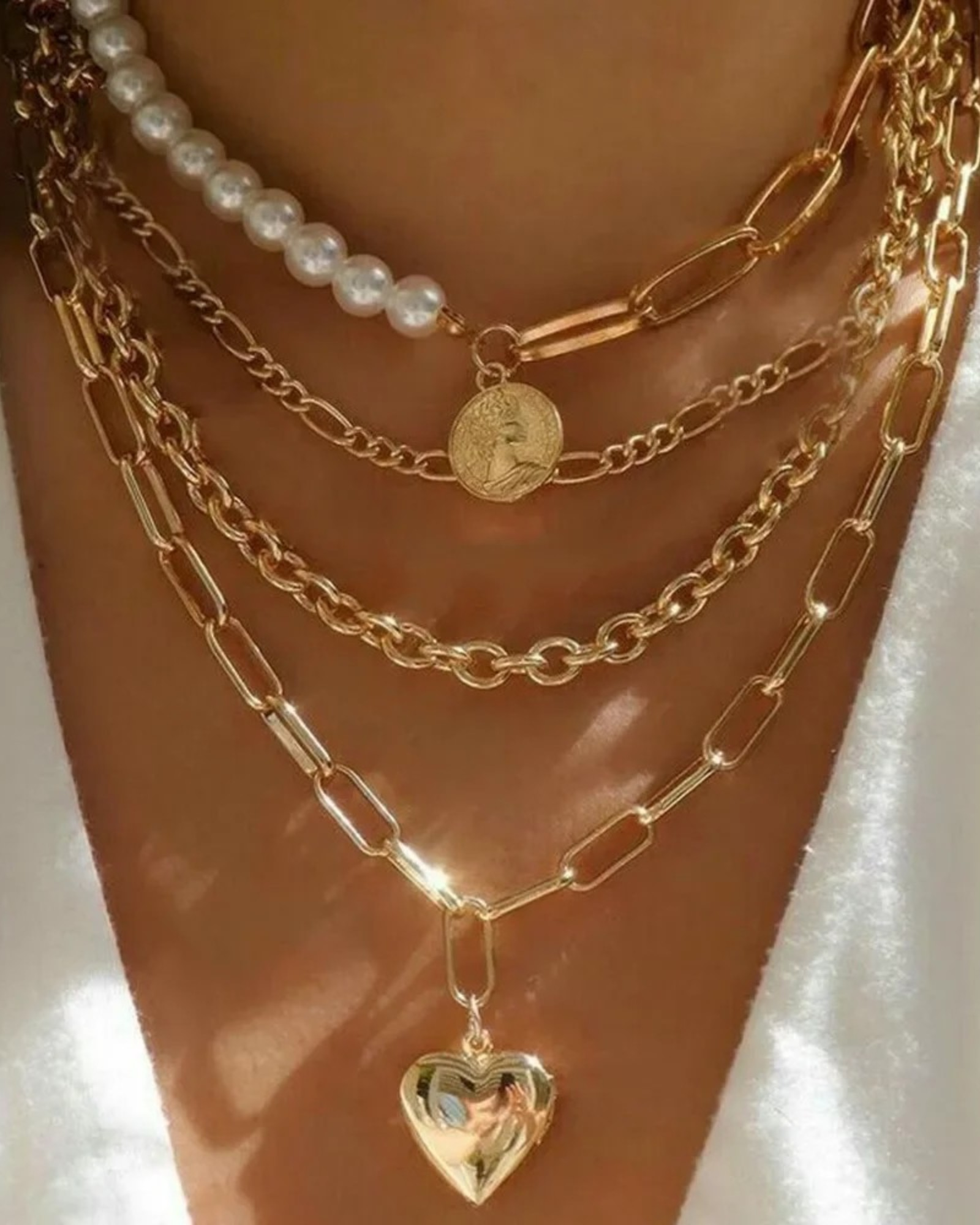 Women wearing a layered gold-tone necklace with pearl-style beads, coin charm, mixed chains, and heart pendant