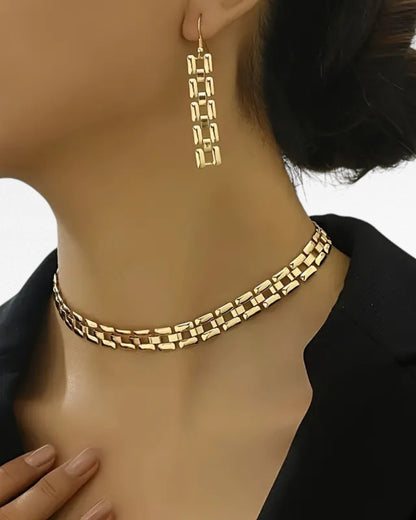 Woman wearing gold-tone geometric link necklace and long drop earrings with black blazer