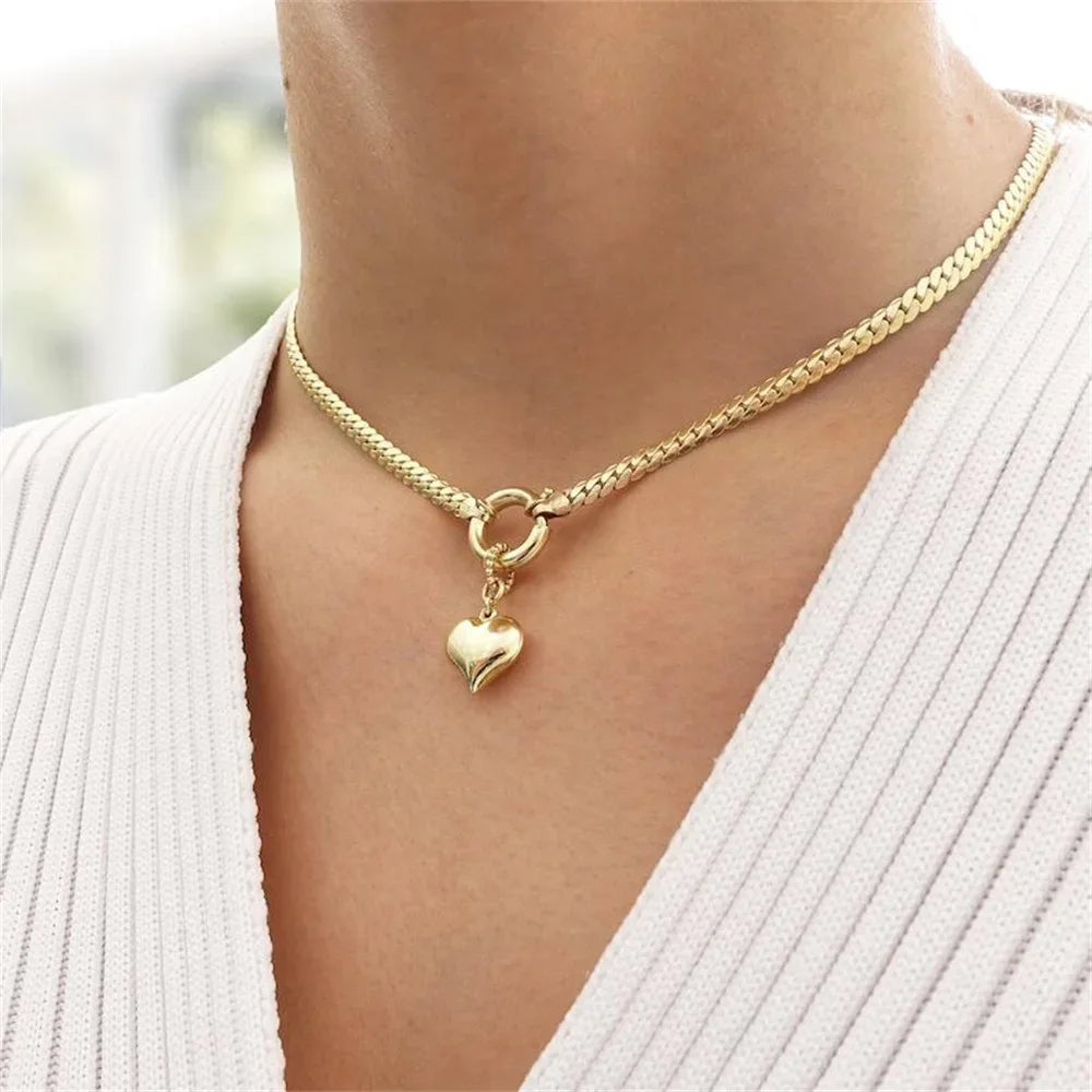Woman wearing a gold-tone curb chain necklace with a heart pendant and circular clasp