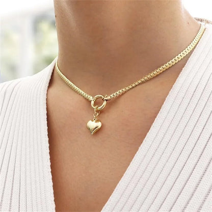 Woman wearing a gold-tone curb chain necklace with a heart pendant and circular clasp
